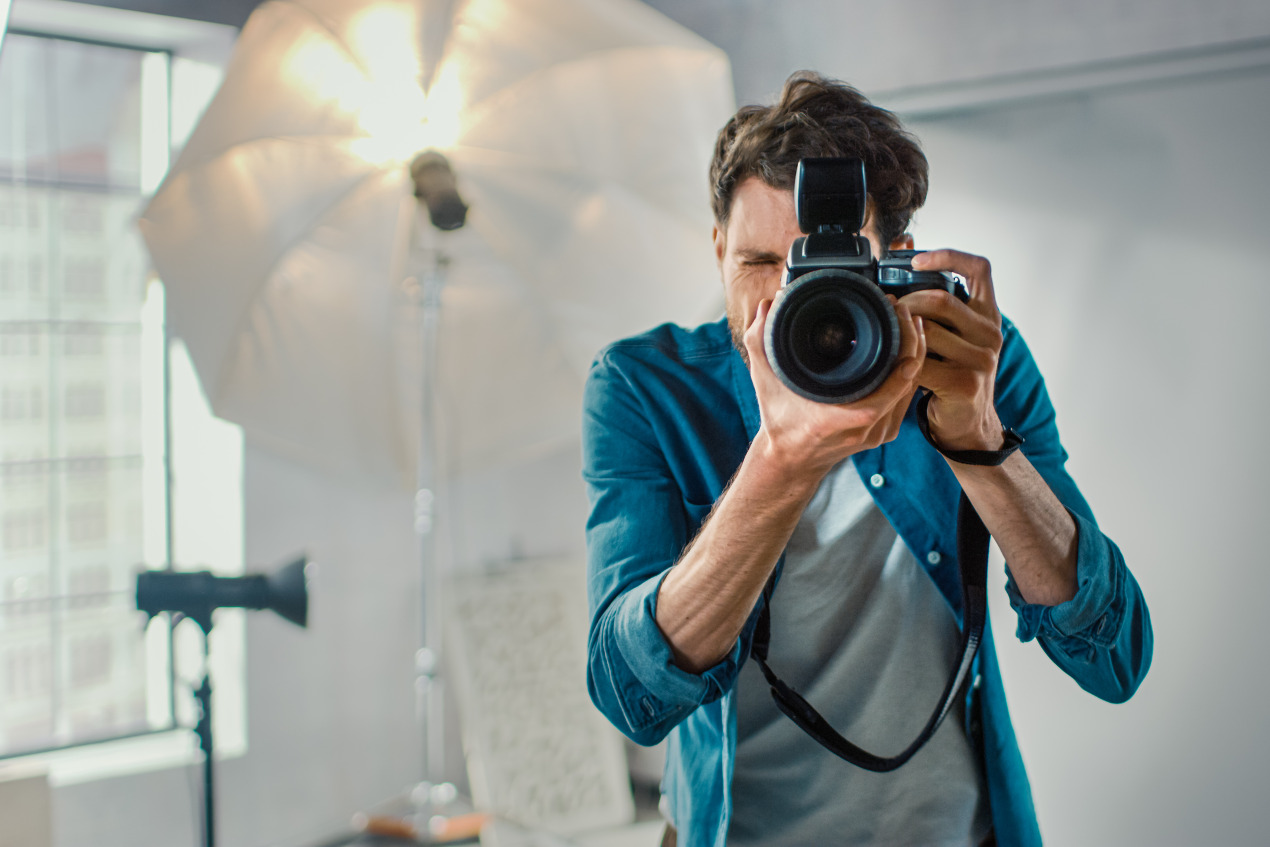 Fotograf steht im Fotostudio und schaut in seine Kamera.