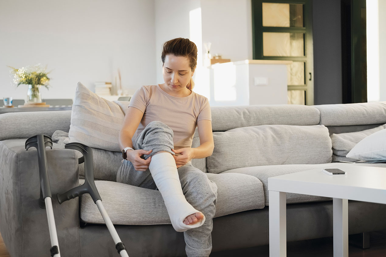 Mann mit Gipsbein sitzt auf dem Sofa und telefoniert.