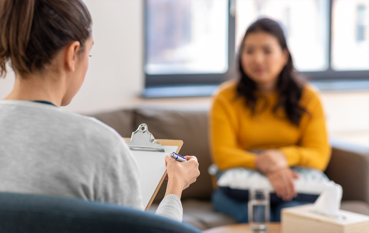 Zwei Frauen bei einem therapeutischen Gespräch. Die Therapeutin macht sich Notizen.