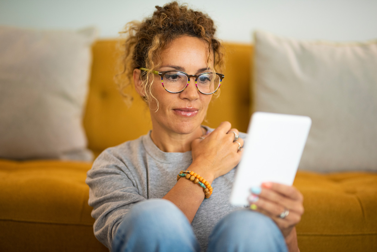 Frau sitzt vor einem Sofa und schaut in ihren Tablet-PC.