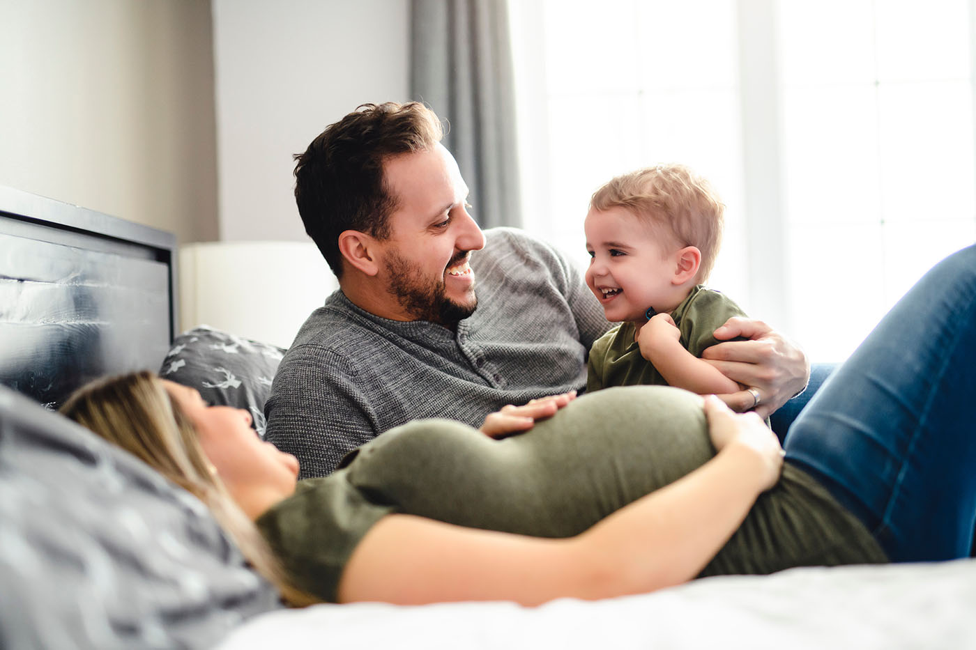 Mutter, Vater, kleines Kind liegen auf dem Bett, Frau ist schwanger