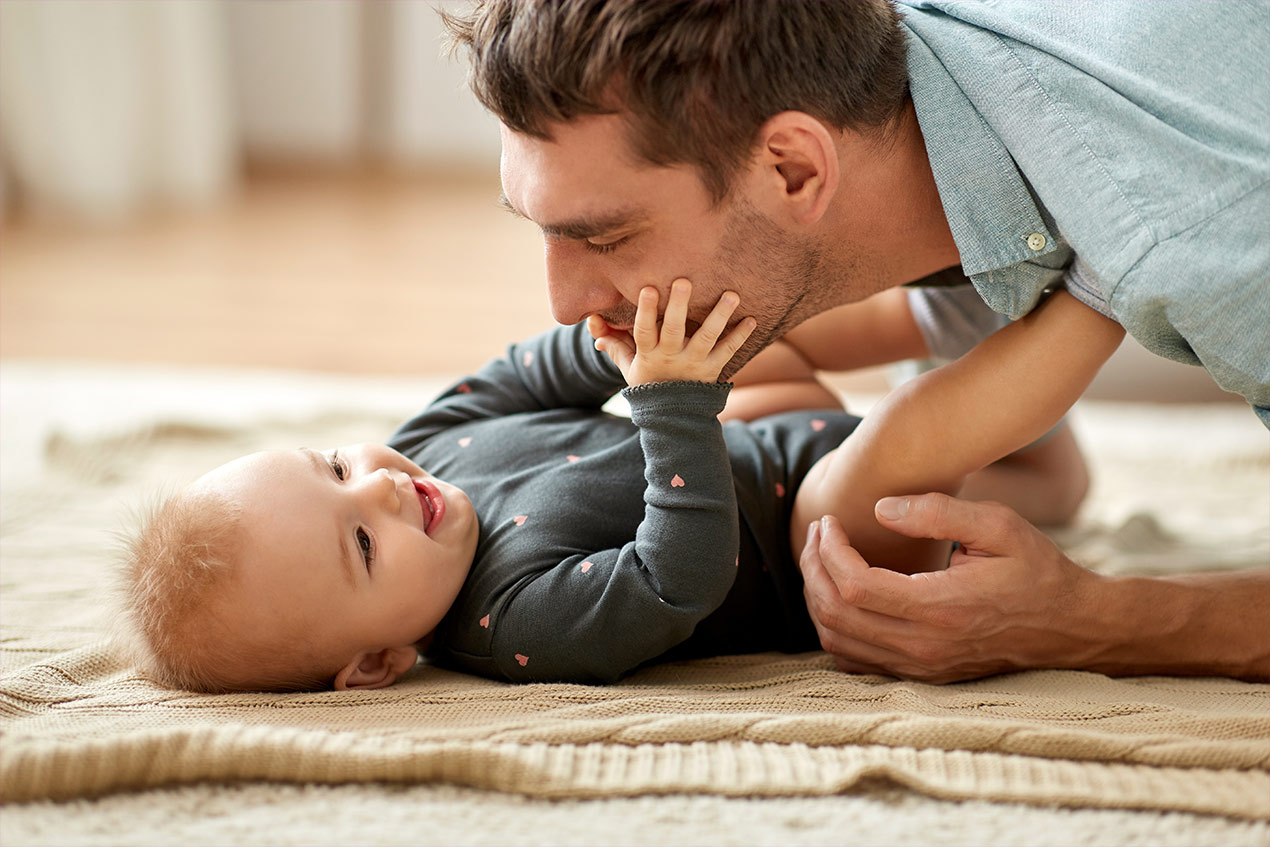 Ein Vater der mit seinem Baby spielt das auf dem Boden liegt