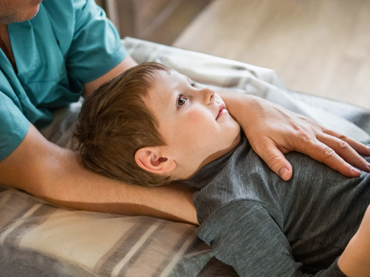 Junge liegt auf einer Behandlungsliege und wird osteopathisch behandelt.