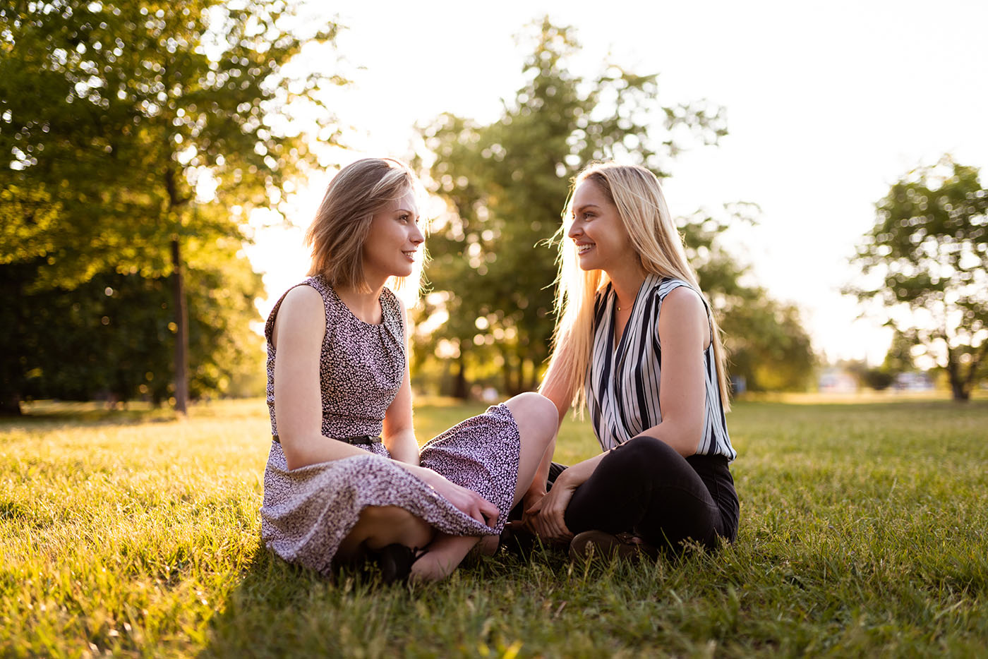 Zwei Frauen sitzen in Sommerkleidern auf einer Wiese.