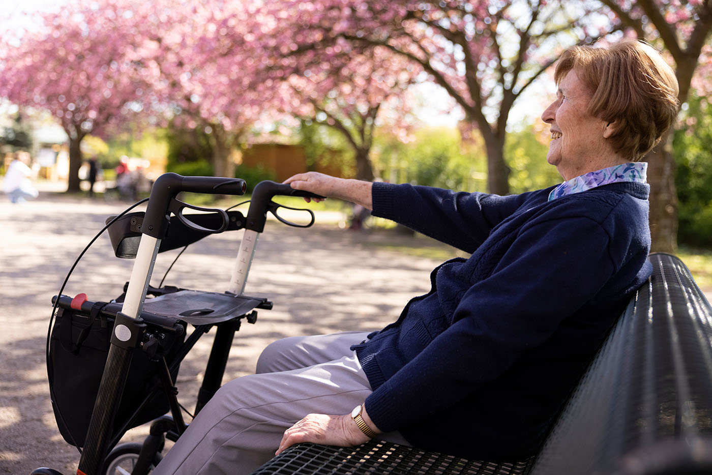 Seniorin sitzt im Park im Frühling auf einer Bank, den Rollator vor sich