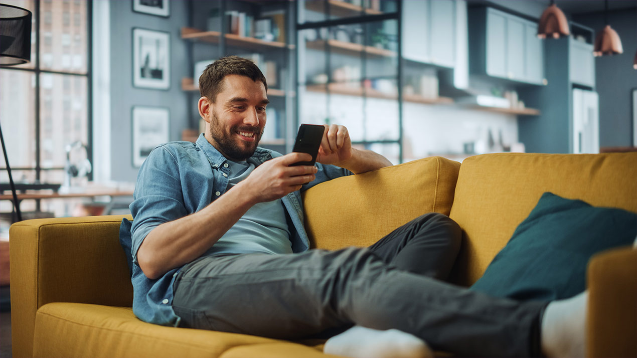 Mann sitzt auf Sofa und nutzt sein Smartphone