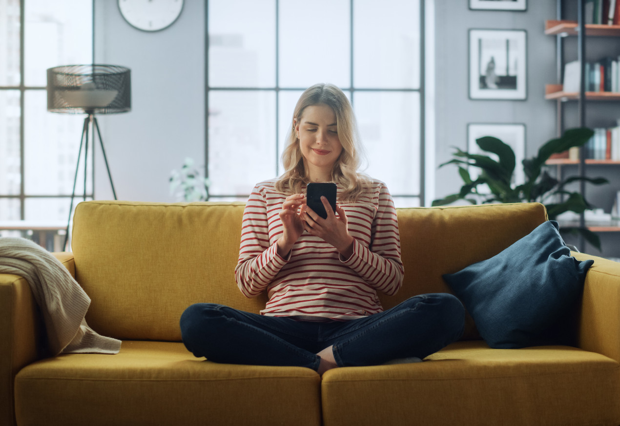 Frau sitzt auf gelbem Sofa und bedient ihr Smartphone