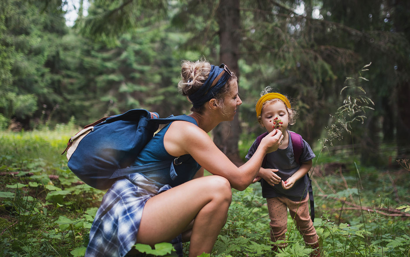 Frau mit einem Kind in der Natur, sie lässt das Kind an einer Pflanze riechen