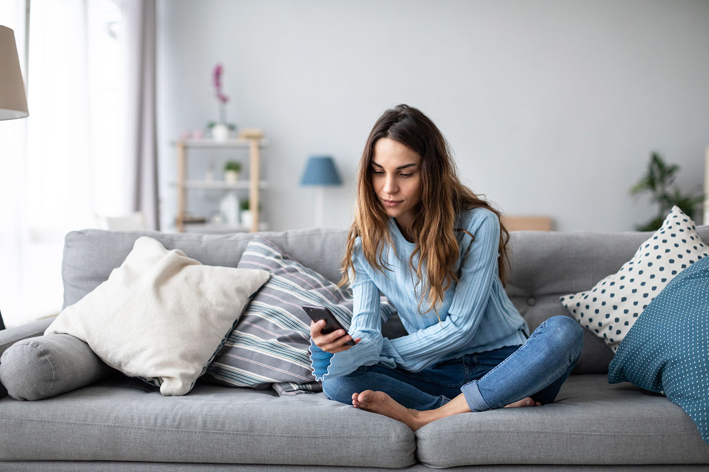 Frau sitzt mit einem Smartphone auf dem Sofa und nimmt am digitalen Nachsorgeprogramm mentalis teil.